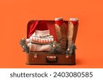 Suitcase with Santa hat, warm clothes, Christmas balls and fir branches on orange background. Winter vacation concept