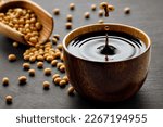 Small photo of soy sauce drop falling from flying soybeans in wooden bowl and created splash on black stone background. Traditional asian condiment. Natural product concept