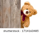 Brown cute teddy bear sneaked behind the old wooden door isolated on white background. Copy space for text and content.