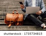  businessman sits on a shoe with laptop and brown leather bag
