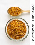 Small photo of Bee pollen granules in a glass bowl and wooden spoon on white background. Superfood, flower nectar, enzymes, honey and wax. Nutrients, amino acids, lipids and vitamins. Flatlay, top view, copy space.