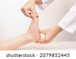 Small photo of Examination of a child by an orthopedist. Cropped shot of female doctor holding a kid's foot in her hands.Pathology of bone structures, flat feet, injury. Foot treatment. Pain from uncomfortable shoes