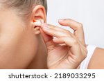 Close up of a young woman putting polyurethane earplugs in her ears with her hand isolated on a white background. Anti-noise earbuds for sleep, rest, travel, airplane