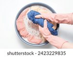 Small photo of Female hands in rubber gloves wring out blue clothes on a background of a basin close up, top view.
