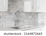 Small photo of A kitchen sink detail shot with white cabinets and a marble subway tile backsplash.