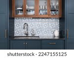 Small photo of A kitchen sink with a beautiful pattern tiled backsplash with a chrome faucet, black granite countertops, and surrounded by blue and wood cabinets.