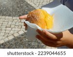 Small photo of Hand holding Bola de Berlim or Berlim Ball, a Portuguese pastry made from a fried donut filled with sweet eggy cream and rolled in crunchy sugar.