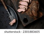 Baked duck fillet. Sliced poultry meat. Piece of duck on fork. Meat onwooden cutting board. Wooden background. View from above. Soft focus. 