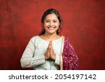 happy smiling Indian girl with traditional ethnic dress in namaste gesture looking at camera - concept of Indian way of greeting.