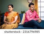 Small photo of Indian angry middle aged couple sitting on sofa in opposite direction at home - concept of conflict, family problems and disagreement