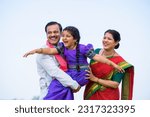 Playful excited indian girl kid while holding by father with mother near farmland - concept of parents support, family bonding and happiness