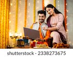 Small photo of Happy young indian couple busy checking laptop during festival celebration at home - concept of sales or offers, buying new apartment and planning