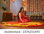 Happy young Indian woman placing diya lamps on decorated flower rangoli for diwali festival celebration at home - concept of festive preparation, traditional culture and spirituality