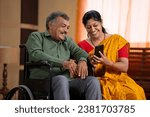 Small photo of Sick or injured laughing Senior husband on wheelchair watching mobile phone with wife at home - concept of family support, companionship and social media sharing or entertainment.