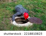 Small photo of A male plumber opened the hatch of a water well and looks inside. Inspection of water pipes and meters.
