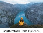 Back view of young woman in yellow jacket standing on top of mountain and looking at Limmernsee Lake. Female sitting on mountain edge and enjoying the beautiful view in Glarus, Switzerland