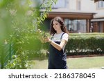 Small photo of Smiling teen girl gardener with curly hair pruning trees in the yard near her house. Young woman with pruner or pruning shears cutting branches at summer garden.