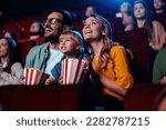 A young joyful couple is with their daughter in the cinema, watching an exciting movie.
