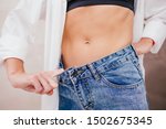 Slim woman in white shirt and black underwear in jeans one size larger is showing successful weight loss. Slim fit concept. Liposuction