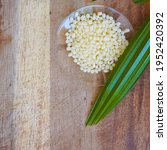 Small photo of Organic Candelilla Wax in Chemical Watch Glass and broadleaf lady palm leaf on wooden background. (Top View)