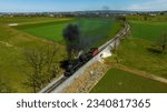 Small photo of A Drone View of a Restored Steam Locomotive and Caboose, Going Over a Small Bridge, Blowing Smoke, on a Sunny Day