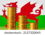 Small photo of Stacks of golden coins forming going down graph on the background of flag of Wales. Concept of regression in finance, investment, income rate of part of GB - Wales