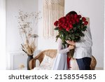 couple in love of man and woman kissing behind big red roses bouquet at home. happy valentines day. engagement day