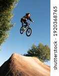Small photo of Caucasian white with long hair boy jumping with BMX bike on a mountain in the field with sand and trees blue sky sunny day