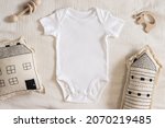 Styled stock photo of clear white baby onesie with scandinavian stitched pillow in the shape of a house and wooden toys on ivory napkin for creating mockup for presentation kids sublimation design