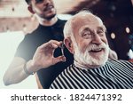 Small photo of An old man looks at the camera while the master cuts his hair in a barbershop. An adult sidoy dede looks at the camera while he gets a stylish haircut.
