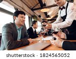 Small photo of The waiter pours wine into a glass to a Chinese business partner. People stipulate business while sitting at a large table in a restaurant.