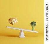 Small photo of broccoli vegetable tipping seesaw with floating berger on opposite end on yellow background. food idea minimal.