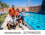 Group of young indian friends having fun standing at pool side resort in hot sunny day. Summer holiday and vacation concept.