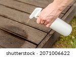 Small photo of Homemade ant repellent spray mixture in bottle. Person hand spraying insect repellent on home terrace wood boards.