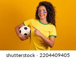 Brazilian supporter. Brazilian woman fan celebrating on soccer or football match on yellow background. Brazil colors.Pointing 