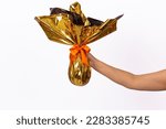 hand holding beautiful chocolate easter egg with golden packaging and orange bow on white background. Easter, chocolate and gift