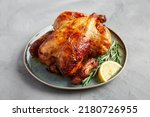 Small photo of Homemade Lemon and Herb Rotisserie Chicken on a Plate on a gray background, side view.