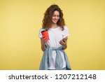 Beautiful shy brunette woman chatting via whatsapp messenger she holding coffee cup, a shot isolated over yellow background