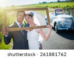 Charming bride and groom posing with a frame for their wedding photos, behind them a lovely country roadd