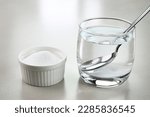 Salt water in a glass cup and salt in a bowl.