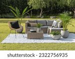 A contemporary outdoor patio space featuring a comfortable sectional couch, armchairs, decorative pillows, lush green grass