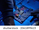 Small photo of Hands in gloves of cellphone technology engineer work on chipset pins of removed microprocessor from smartphone motherboard with soldering iron and hot air heater. macro photo, Selective focus