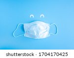 Small photo of Disposable medical mask on blue background with white paper eyes. Smiling cut off face with medical mask. Stop the spread of coronavirus, self-defense. Copy space