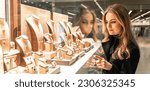 Small photo of Pretty woman looking at jewelry in store window. Customer near jewellery. Dreamy long haired blonde girl chooses silver, gold, diamonds, precious stones. Purchaser