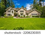 Small photo of Beautiful custom built craftsman style home three car garage with wooden doors lush landscaping with spring foliage and shadows dappling the yard