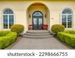 Small photo of Large estate home on lush green grass landscaping blue sky elegant house has yellow paint three car garage rounded shape heavy wooden front door arched doorway and brick trim