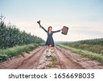 Small photo of happy romantic girl travels on the road with a suitcase. woman in a blooper and with a bouquet of color joyful raised her hands up. concept vacation, freedom