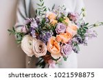 Very nice young woman holding big and beautiful colourful flower wedding bouquet with purple carnations and mattiolas, cream David Austin roses, ranunculus and pistachios