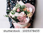 Very nice florist woman holding a beautiful colourful blossoming flower bouquet of fresh Quicksand roses, carnations, ranunculus, peony, pistachio leaves on the grey wall background