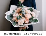 Very nice young woman holding big and beautiful bouquet of fresh roses, carnations, eucalyptus flowers in pastel pink colors, cropped photo, bouquet close up